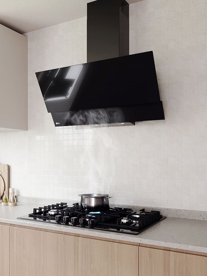 Modern kitchen interior featuring an angled glass hood above a gas cooktop with a pot, against a white tile wall.
