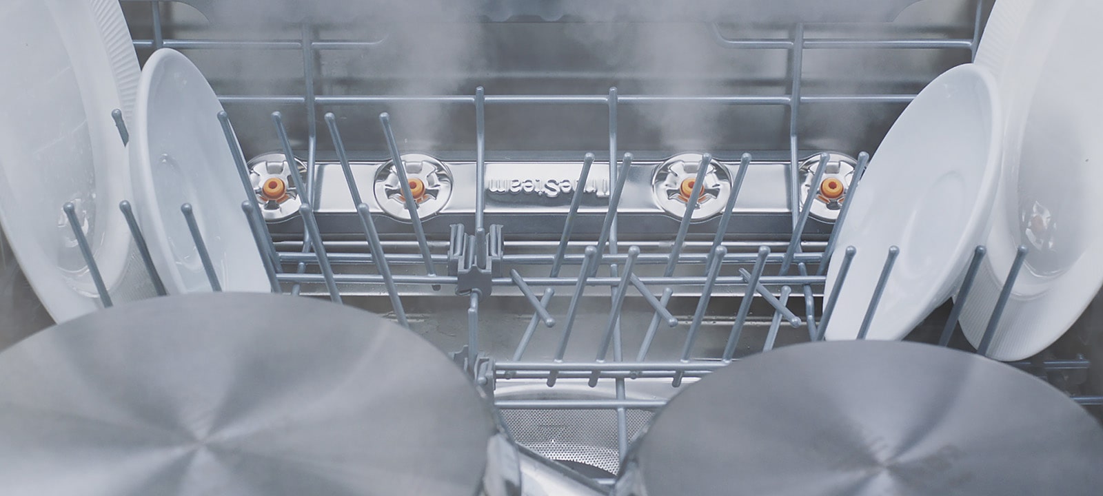 Footage of close-up view of various kinds of dishes being steam-washed inside dishwasher.