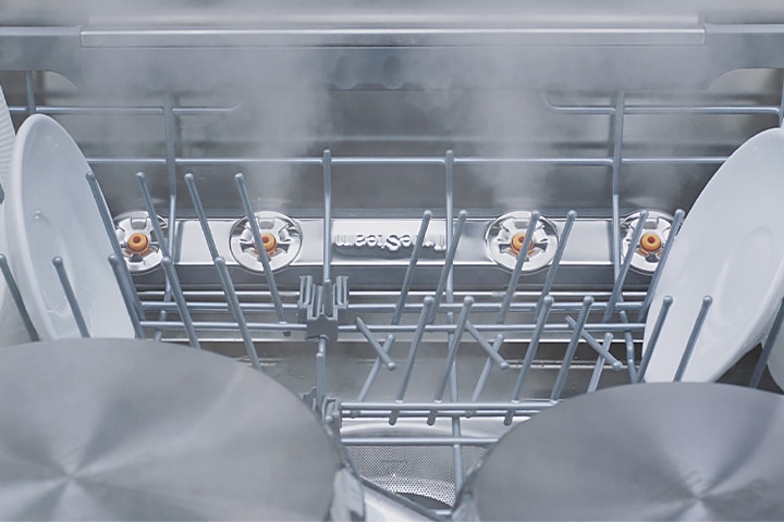 Footage of close-up view of various kinds of dishes being steam-washed inside dishwasher.
