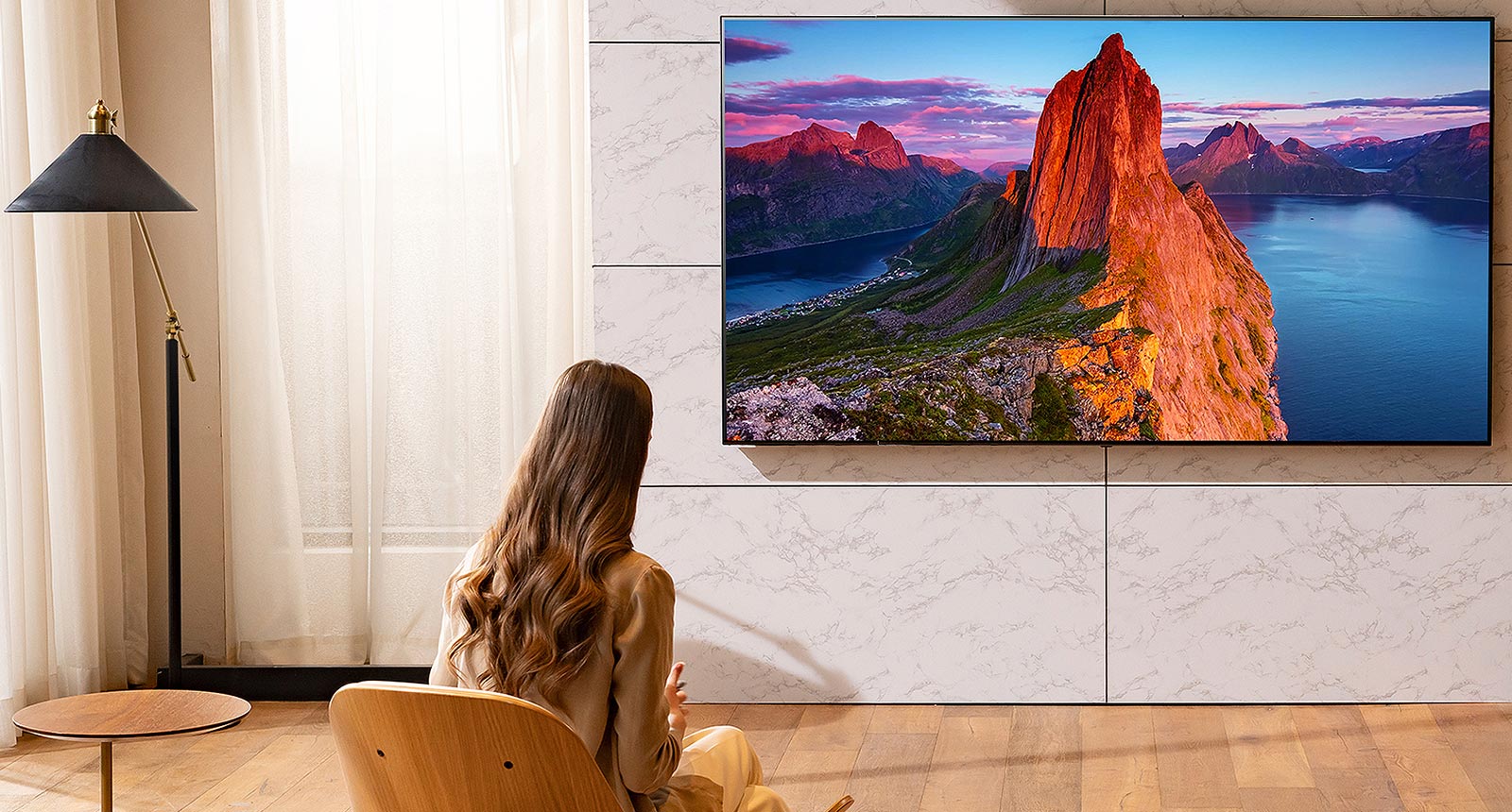 A woman is watching TV in the living room. Landscape scenery is on the screen.