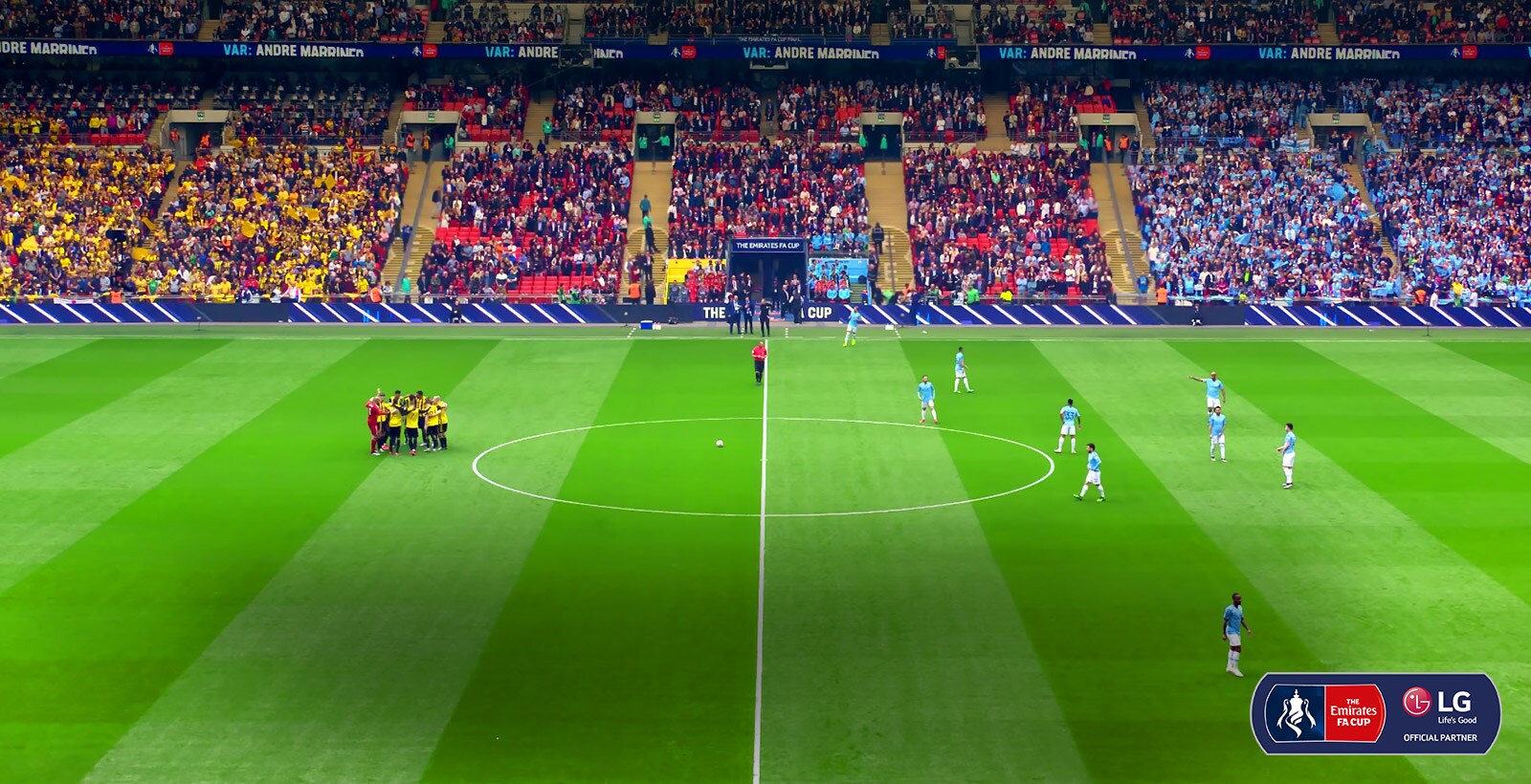 Wide shot of a soccer pitch. The players are gathering in the middle to prepare for the match.