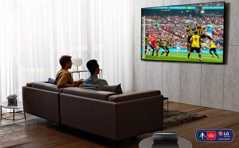 Two men are watching a sports game on TV in the living room with Bluetooth rear speakers.