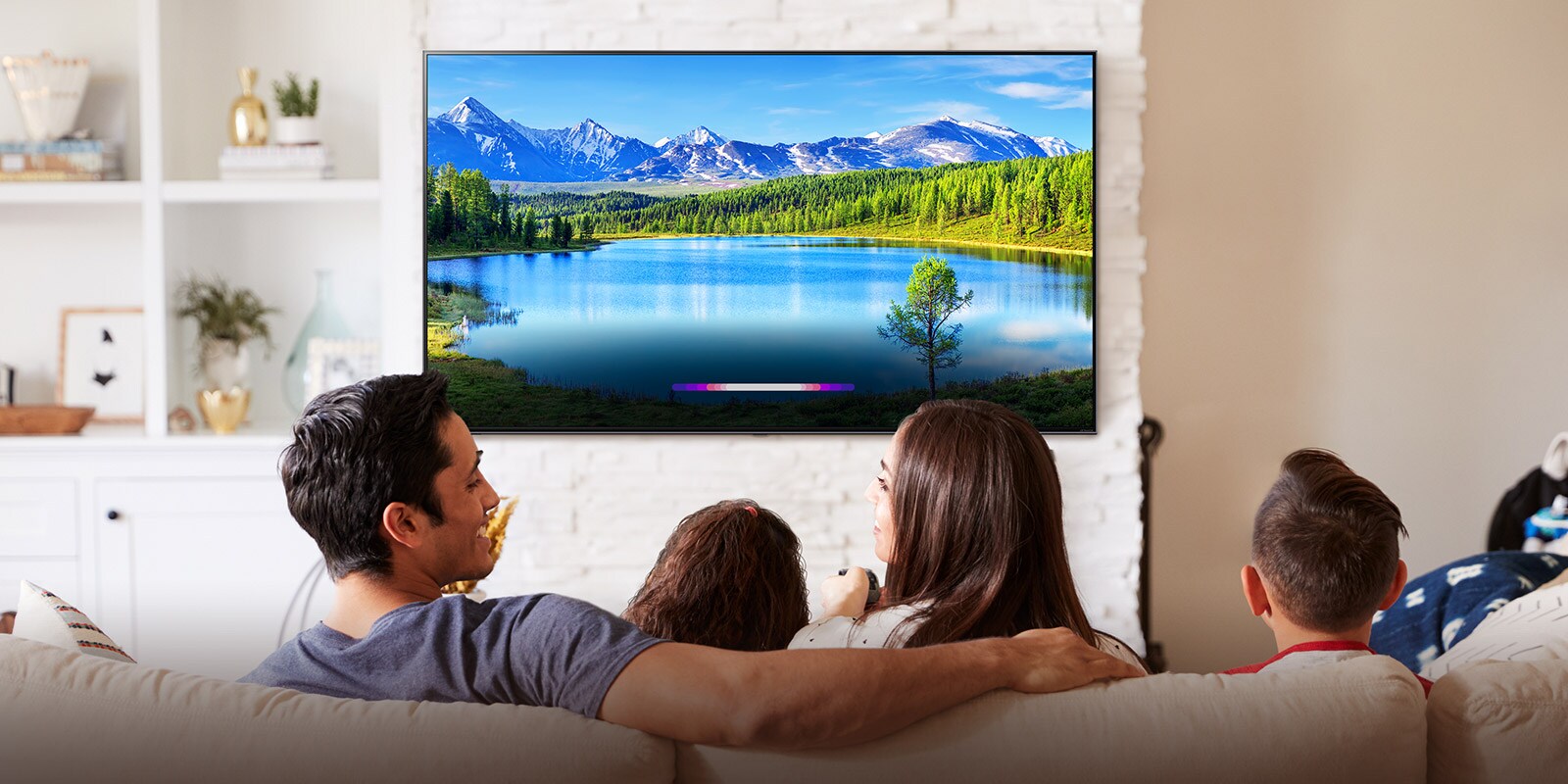 Family in bright living room looking at landscape on wall-mounted TV