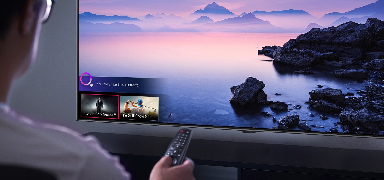 Closeup of a man choosing what to watch on TV with a remote control, with TV showing landscape.