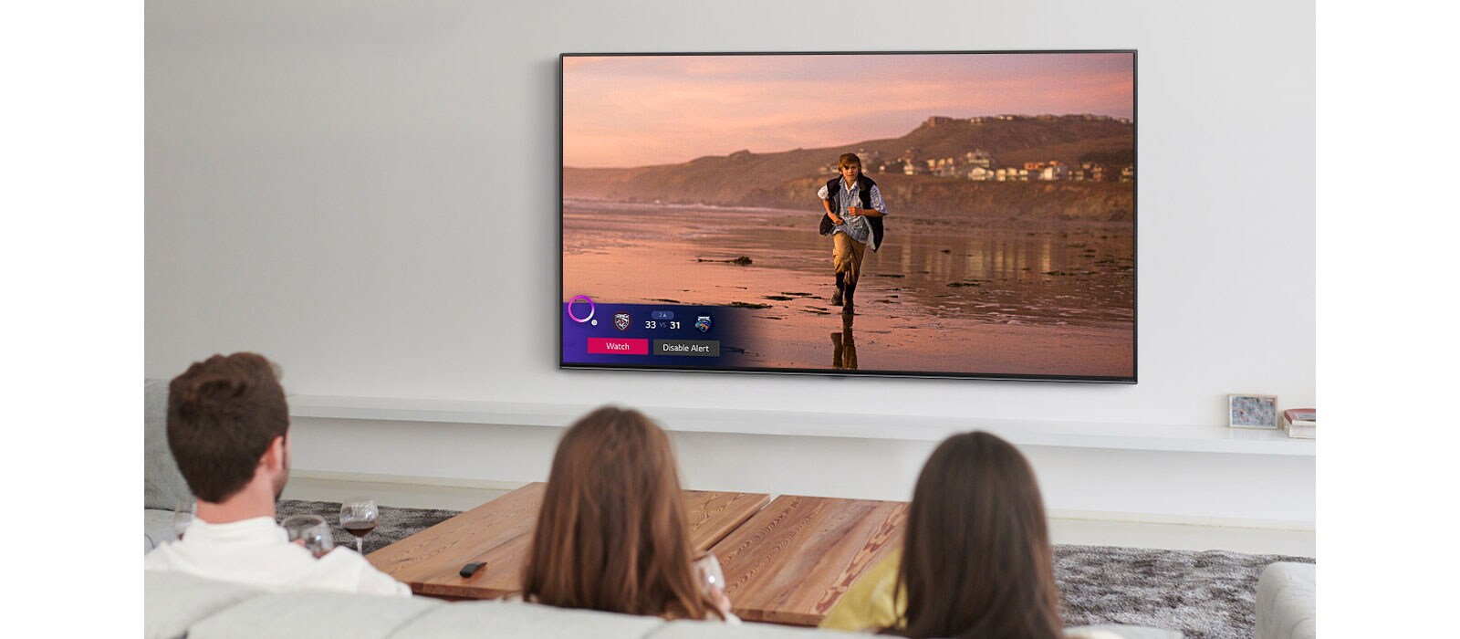 Three people watching TV screen showing a scene from a fantasy movie with a Sports Alert.