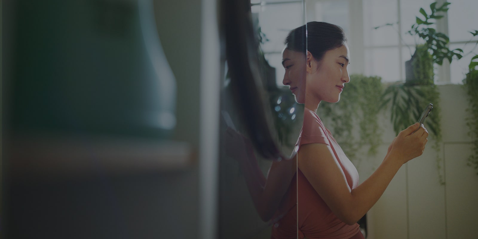 Image shows a woman standing next to a washtower, looking into her phone while smiling.
