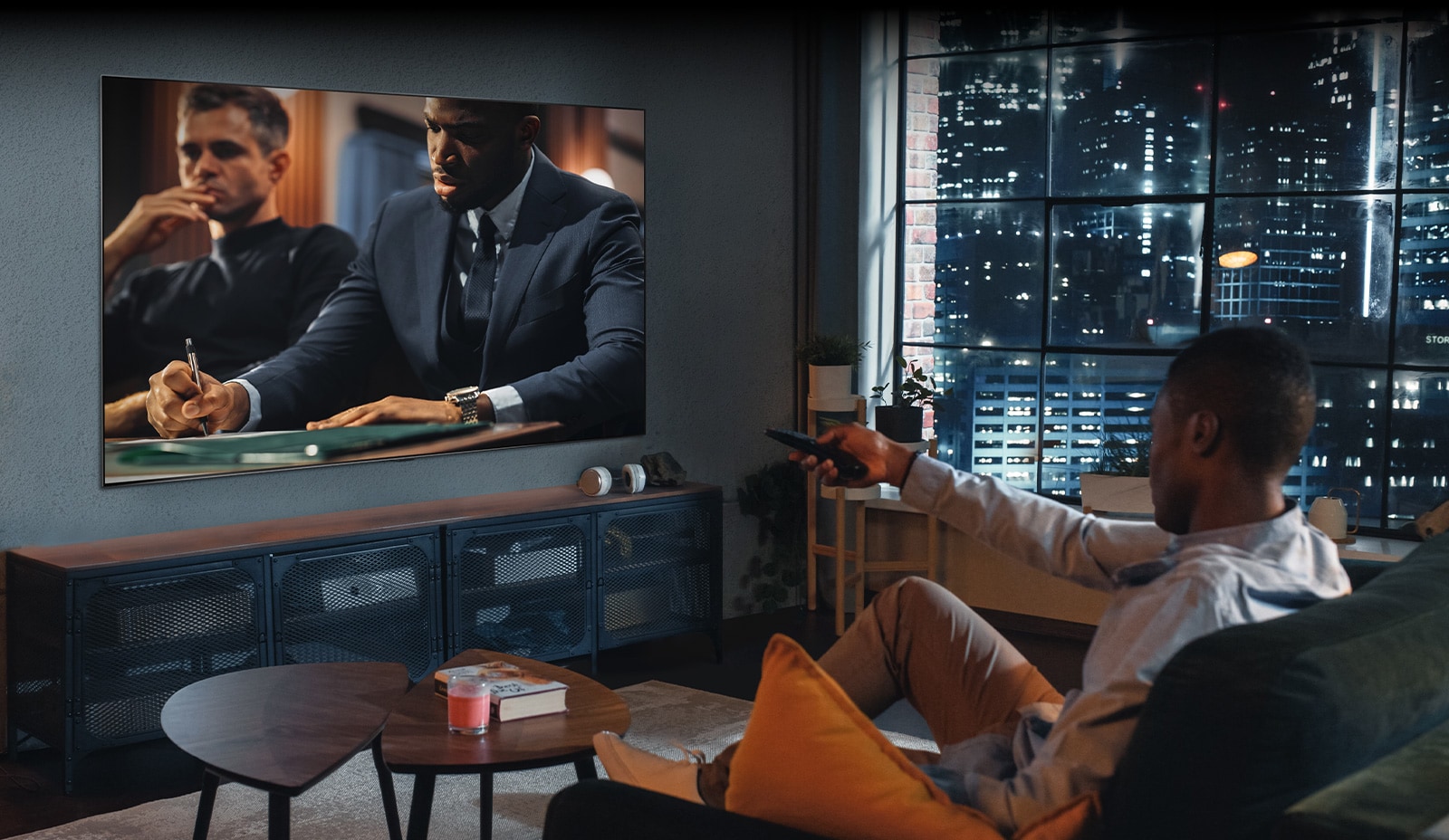 A man is sitting on the sofa watching TV. The man has a remote control in his hand, and TV shows a scene from the movie.