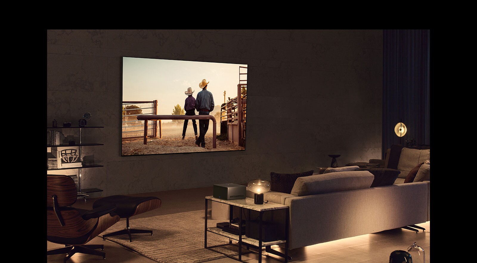 A cowboy movie plays on a wall-mounted LG OLED TV in a cozy living space in the evening. There are no wires surrounding the smart TV. The Wireless Connect Box sits neatly on a side table. The image slides out to show a different living space with a picturesque scene of a car on a highway on the LG OLED TV screen. The smart TV is on a floor stand and there are no wires surrounding it. Its Wireless Connect Box sits neatly on a side table.