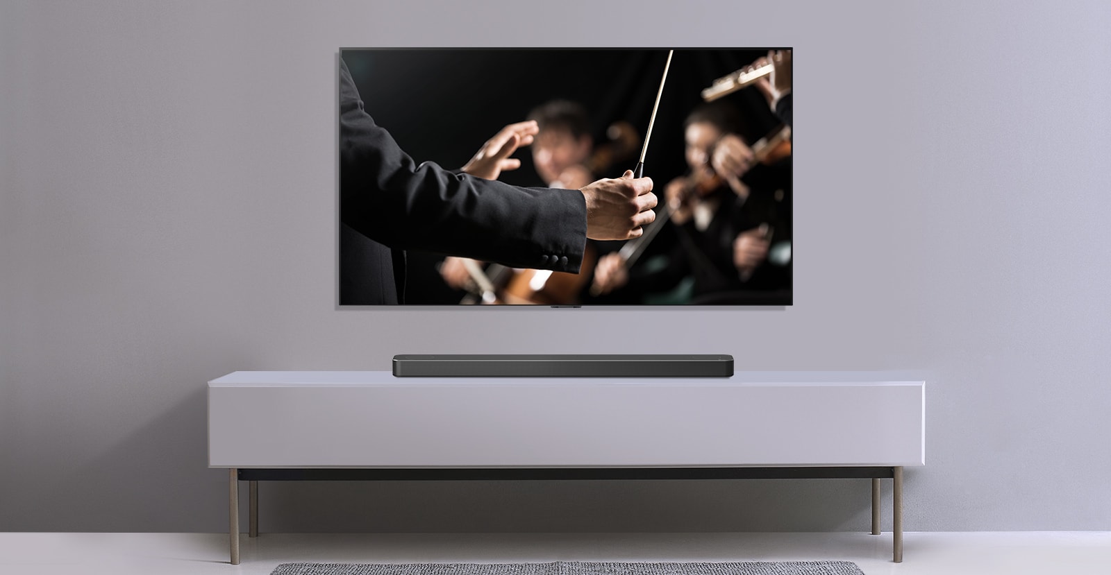 A TV is shown on a gray wall and LG Soundbar below it on a gray shelf. TV shows a conductor conducting an orchestra. 