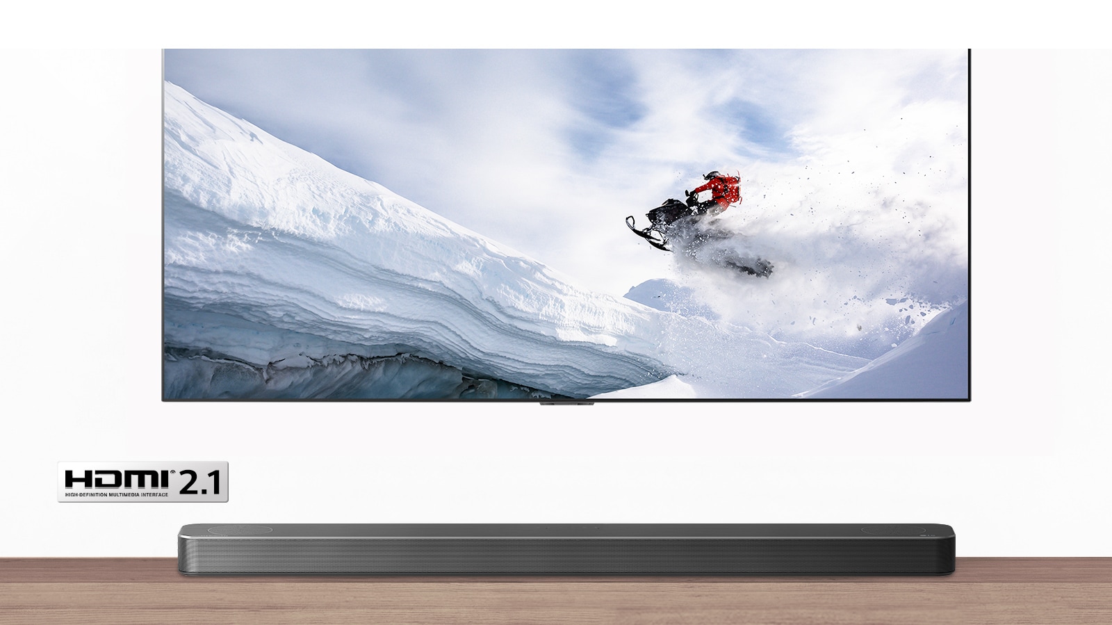 TV and Soundbar are seen from the front. TV shows man riding snowmobile in the snowy mountains. HDMI 2.1 logo is below TV. 