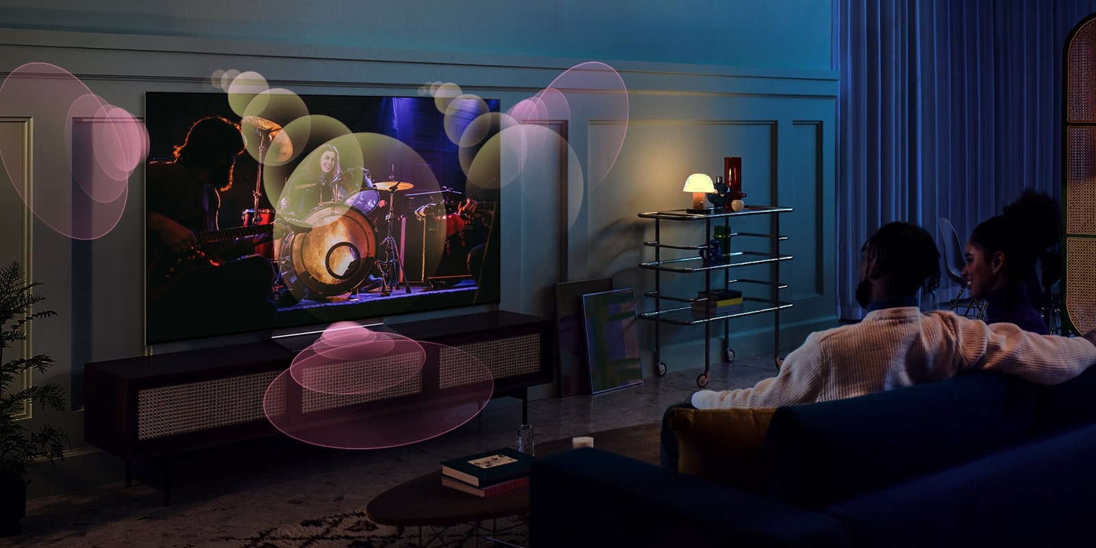People sit on a couch watching a concert with bubbles depicting surround sound around them.