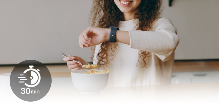 Una mujer sentada a la mesa mira su reloj de pulsera durante una comida ligera. Y un icono con 30 minutos escrito.
