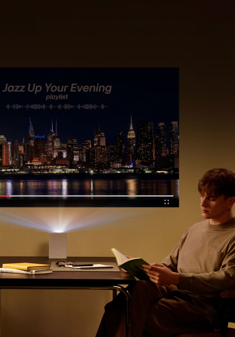 Hombre leyendo un libro con proyección LG CineBeam de fondo.