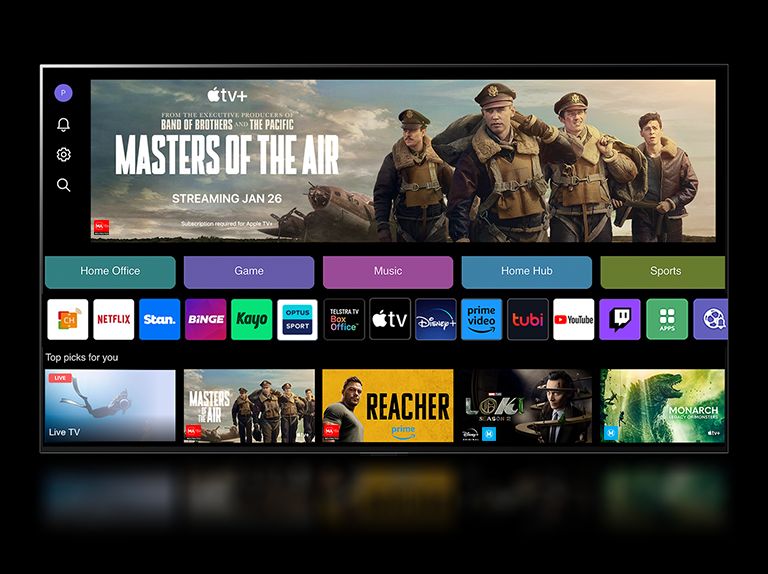 Un primer plano de la pantalla de un televisor LG que muestra los botones Home Office, Game y Music sobre un cartel de Masters of the Air se aleja para mostrar el televisor montado en una pared de una sala de estar. Los siguientes logotipos se muestran en la pantalla del televisor en la imagen: LG Channels, Netflix, Prime Video, Disney TV, Apple TV, YouTube, Spotify, Twitch, GeForce Now y Udemy.