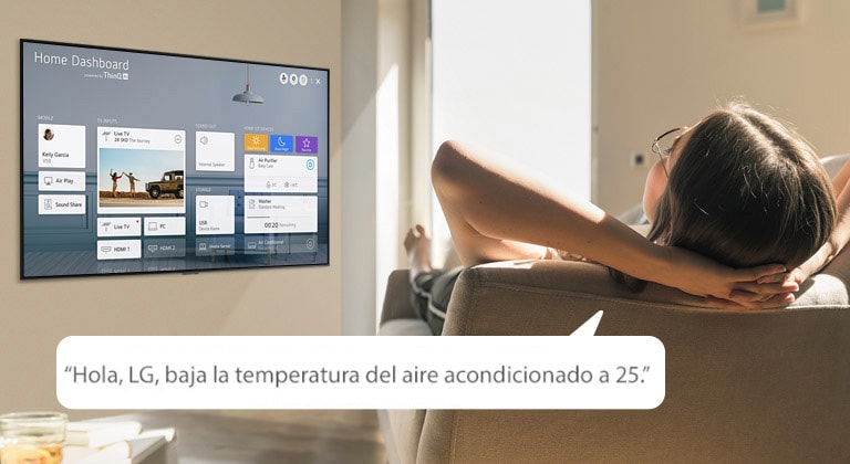 Mujer recostada en un sofá diciéndole a la TV que baje la temperatura con el Panel de inicio en la pantalla de la TV