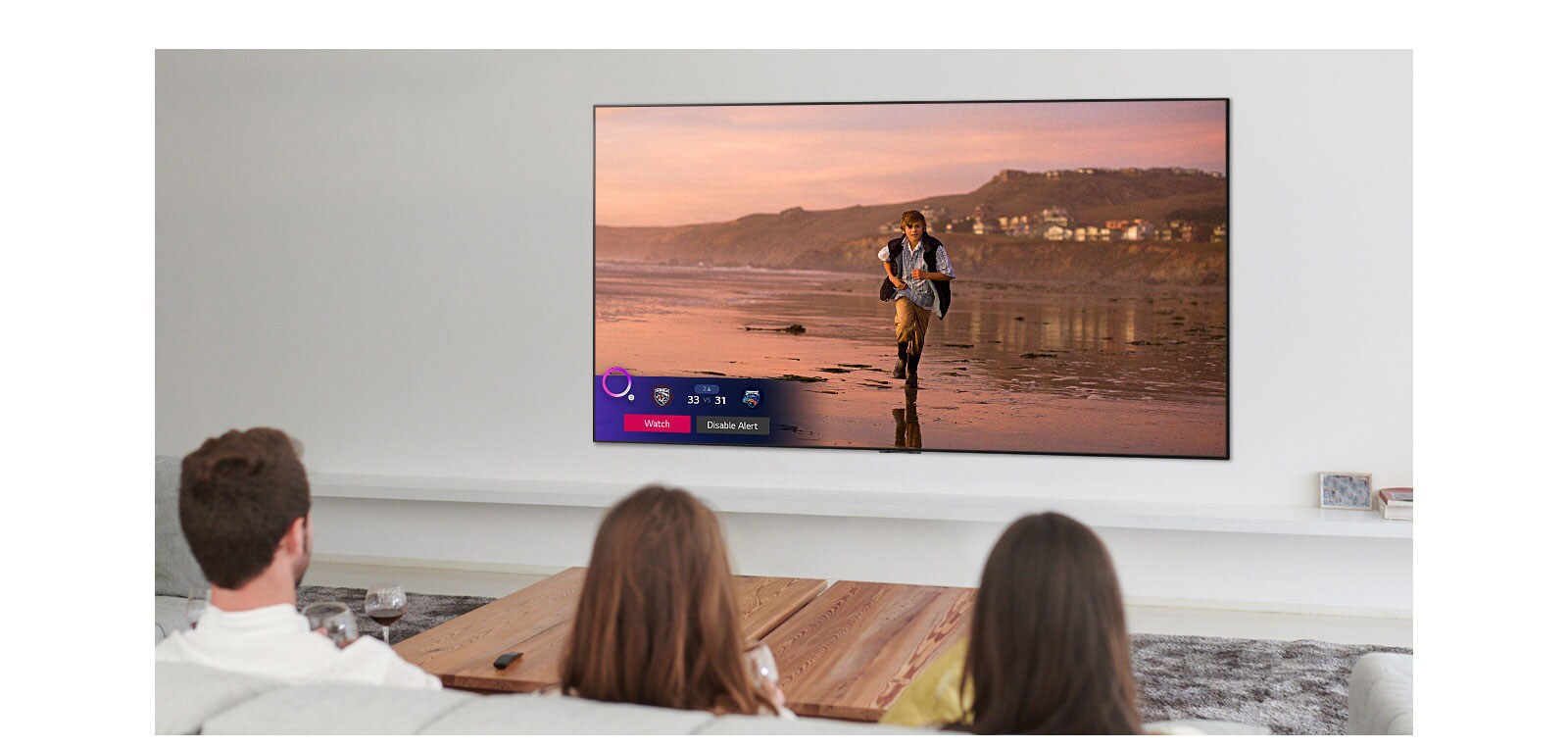 Tres personas mirando la pantalla de TV que muestra una escena de una película de fantasía con un Alerta de deportes