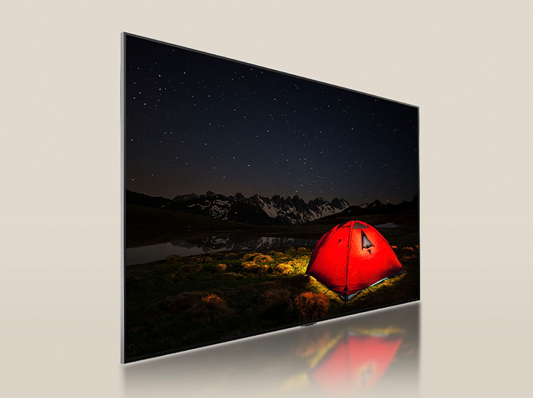 Televisor LG con pantalla tenue que muestra una noche oscura con una carpa de color rojo brillante. Un panel de luz de fondo azul se divide detrás del televisor. Pequeños bloques de atenuación se encuentran dispersos por el panel. Luego, el panel y el televisor se fusionan para hacer que la pantalla se vuelva más brillante y clara.