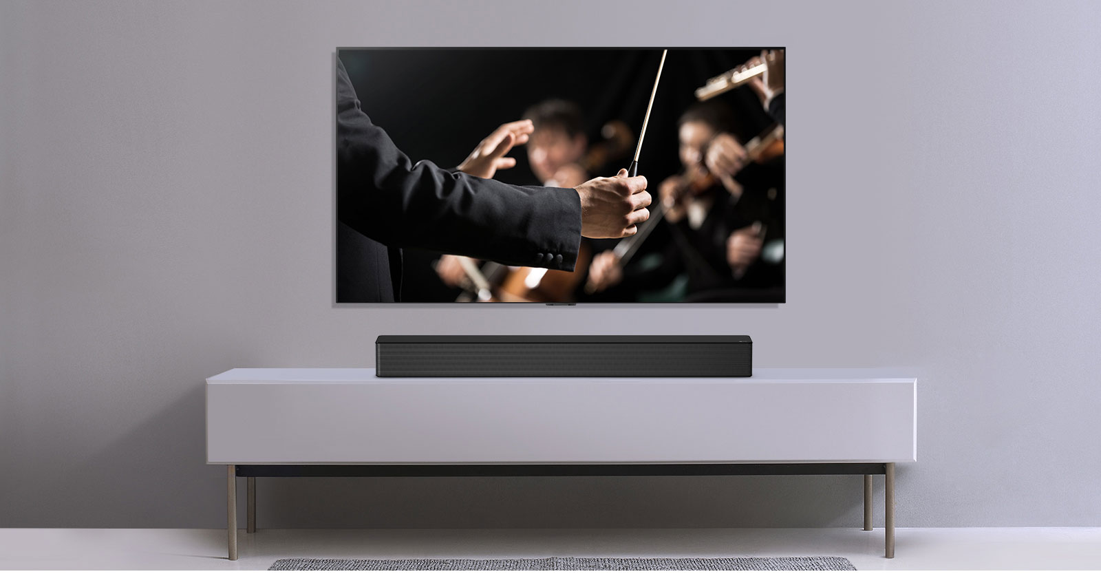 TV en una pared gris y barra de sonido LG abajo en un estante gris. La TV tiene un director dirigiendo una orquesta.