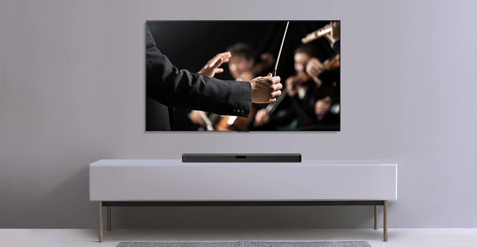 LaTV en una pared gris y barra de sonido LG abajo en un estante gris. La TV tiene un director de orquesta.