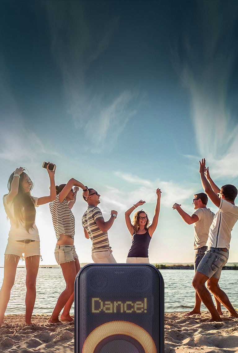 Primer plano de la iluminación de píxeles dinámica. ¡Muestra el baile! Texto. Abajo, la iluminación anular multicolor naranja está encendida. Detrás del parlante, la gente está bailando en la playa.