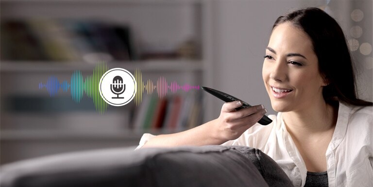 Una mujer está controlando la televisión hablando con un control remoto que tiene reconocimiento de voz.