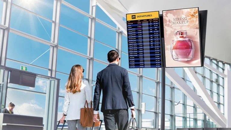 Un hombre y una mujer están consultando la hora de salida del vuelo a través de la pantalla de señalización instalada en el aeropuerto. La pantalla con revestimiento antirreflejante tiene un pequeño reflejo de la luz del sol.