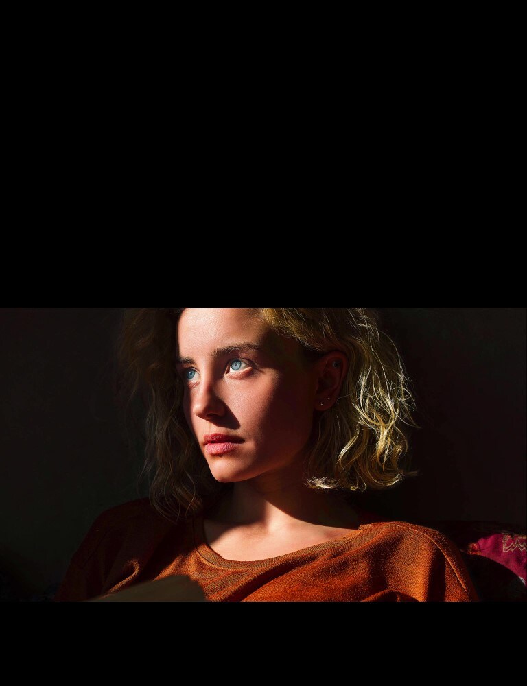 Una mujer con ojos azules penetrantes y una remera de color naranja tostado en un ambiente oscuro. Líneas rojas que ilustran las refinaciones introducidas por la IA le cubren parte de la cara, que es brillante y detallada frente al resto de la imagen, que se ve menos colorida.