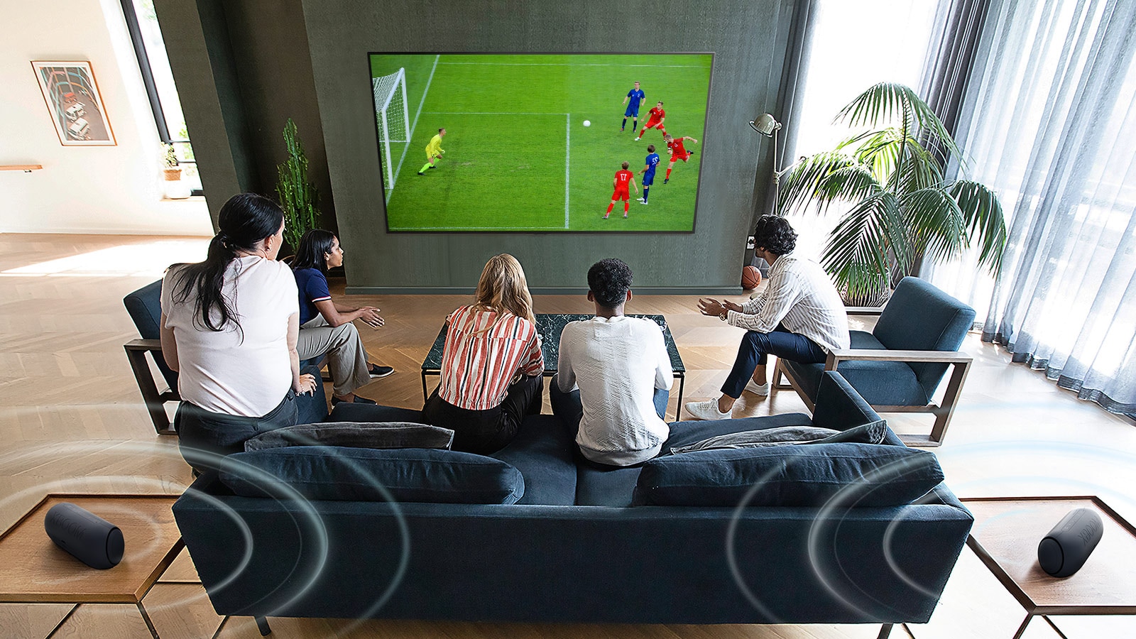 5 personas reunidas frente a un televisor de pantalla plana montado en la pared viendo un partido de fútbol.