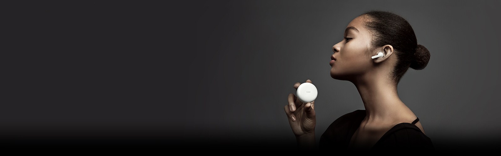 Vista lateral de una mujer sosteniendo TONE Free de LG contra un fondo oscuro.