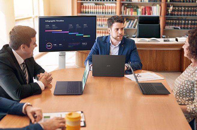 "Cuatro personas están sentadas alrededor de un escritorio, teniendo una reunión usando un LG Smart Monitor Swing.