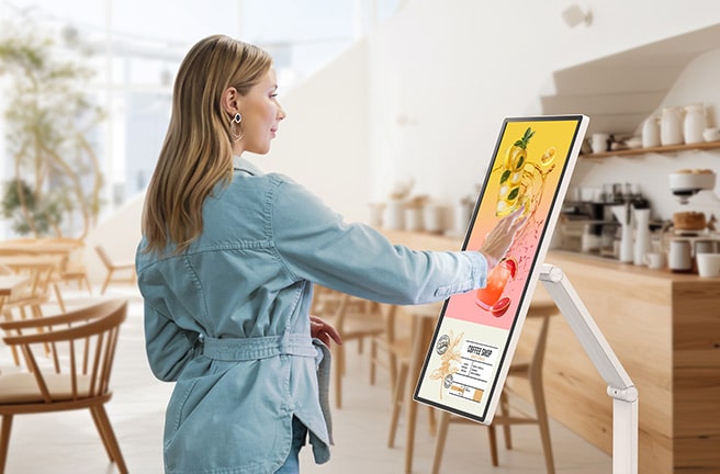 Una mujer está mirando un banner de evento mostrado en un LG Smart Monitor Swing en un café