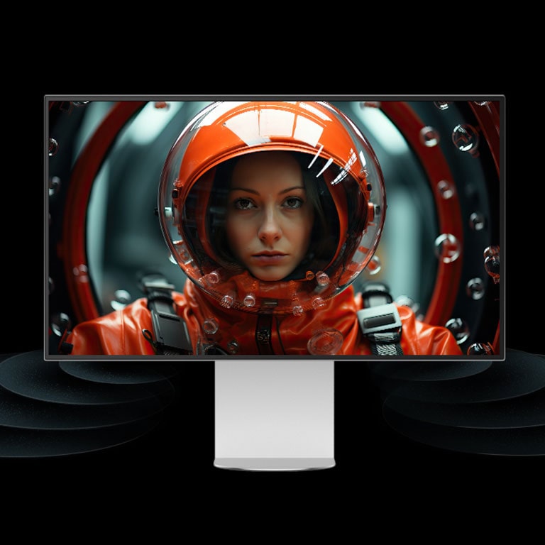 Un monitor UltraFine se coloca en un espacio virtual con ondas sonoras que provienen de la parte inferior del monitor y avanzan. En la pantalla, una mujer con un traje espacial rojo mira hacia adelante.