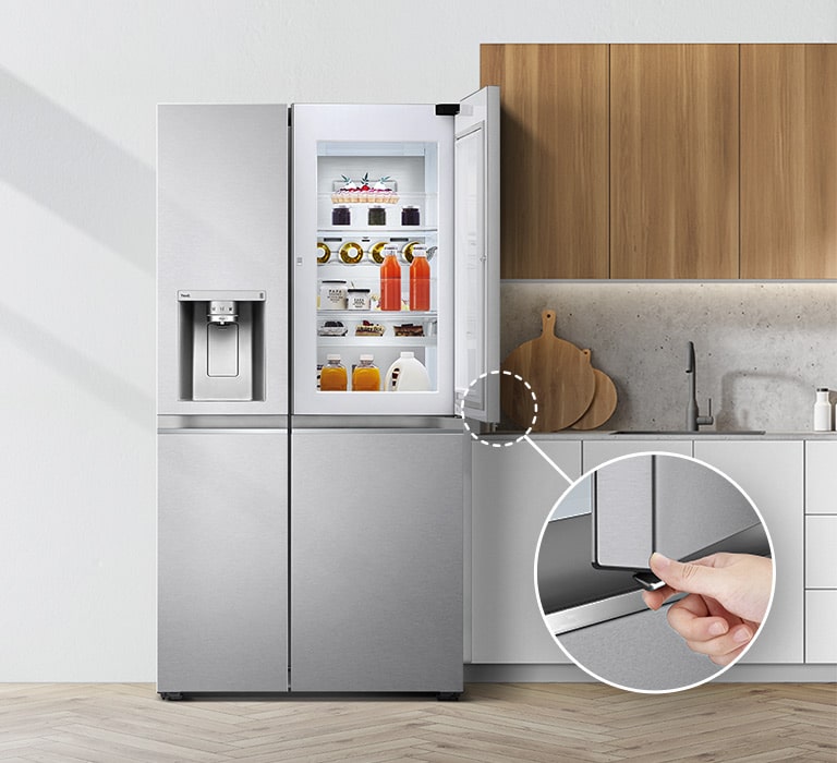 A front view of the refrigerator installed in a kitchen. The upper right door is open and there is a circle and a line that leads to a larger circle that shows an enlarged view of the button in the lower left corner of the open door that has a hidden opening button.