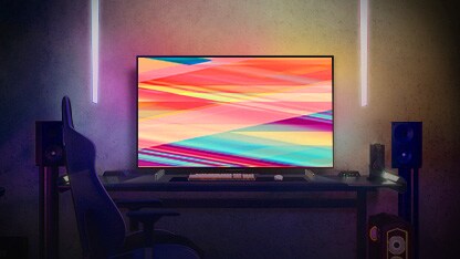 Un TV LG OLED C2 está en una habitación con iluminación nocturna cálida, con sofás, muchos cojines, una lámpara, una mesita auxiliar y una planta.