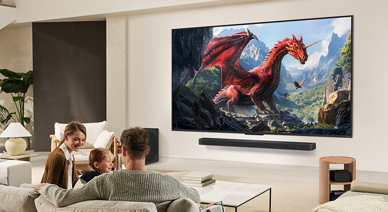 Perekond istub diivanil ja vaatab LG Soundbari kohale seinale kinnitatud LG QNED TV telerit, millel on kujutatud kahte delfiini ja väike tüdruk osutab ekraanile. 