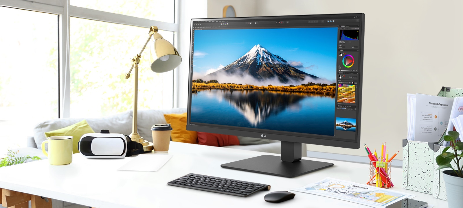 Töölaual on ülipeen monitor, mis kuvab Photoshopi tööd. Monitori kõrval on laualamp, hiir, paber ja värvilised pliiatsid.
