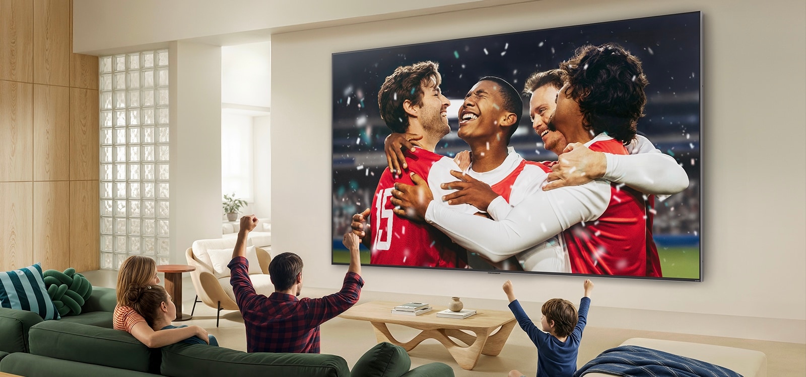 LG QNED evo AI Mini LED QNED90 Ultra Big TV on paigaldatud valgusküllase elutoa seinale ning kuvab laial ekraanil elavate värvide ja viimistletud pildikvaliteediga spordipidu staadionil, samal ajal kui diivanitel istuv perekond koos juubeldab.