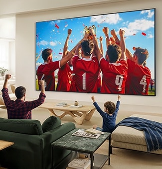 LG QNED evo AI QNED85 Mini LED Ultra Big TV on elutoas seinale paigaldatud ning kuvab spordivõidu tähistamist erksate värvide ja viimistletud pildikvaliteediga laial ekraanil, samal ajal kui diivanitel istuv perekond koos juubeldab.