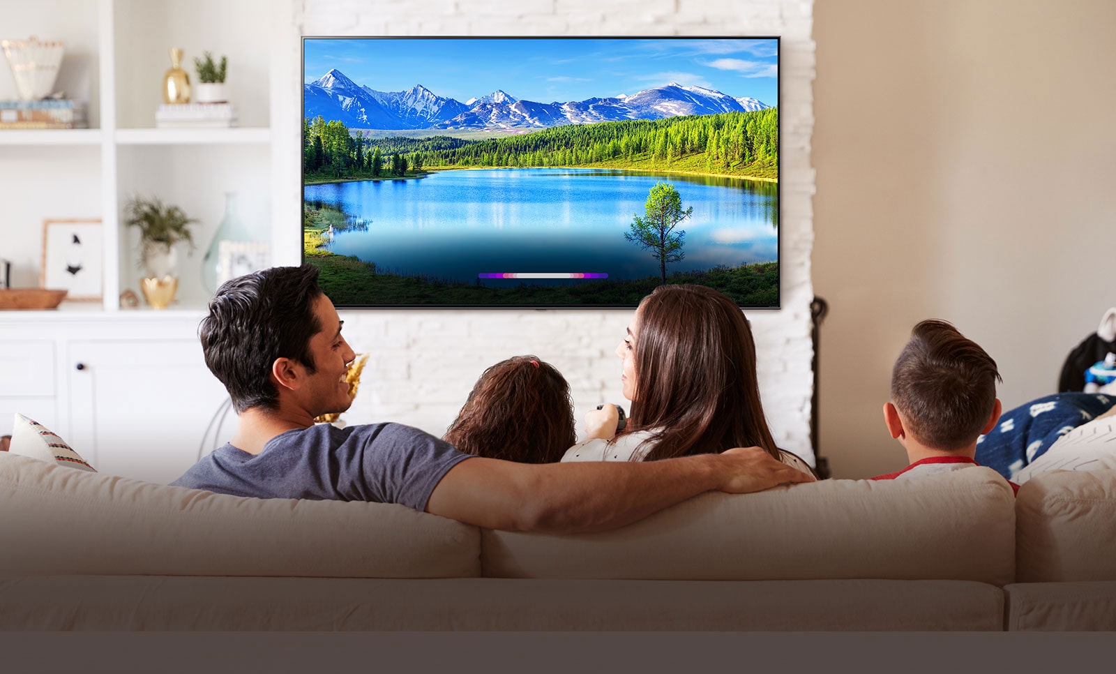 Heledas elutoas seinale kinnitatud telerist maastikupilti vaatav perekond