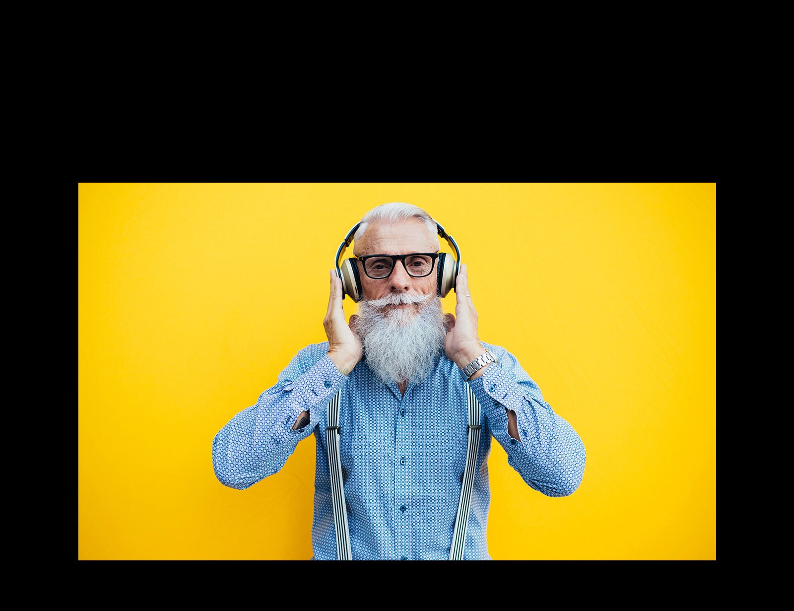 Vanaisa seisab kollase seina ees, kõrvaklapid peas.