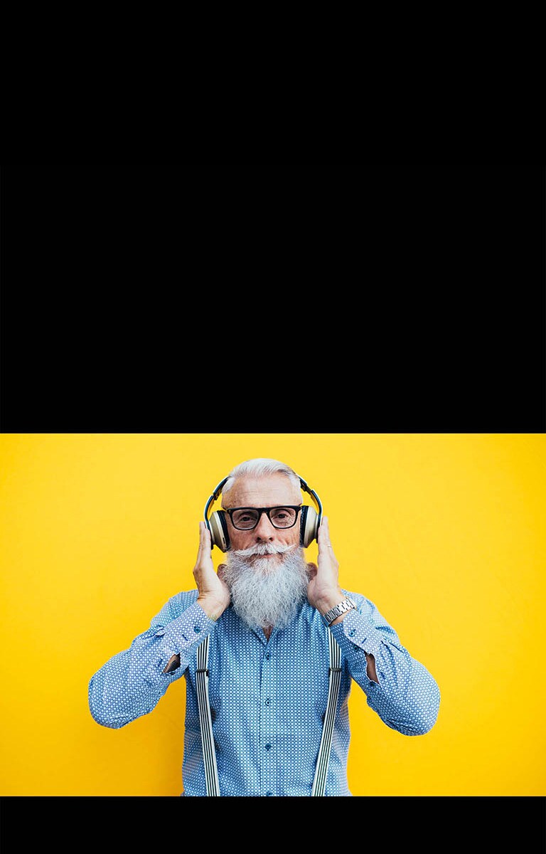 Vanaisa seisab kollase seina ees, kõrvaklapid peas.