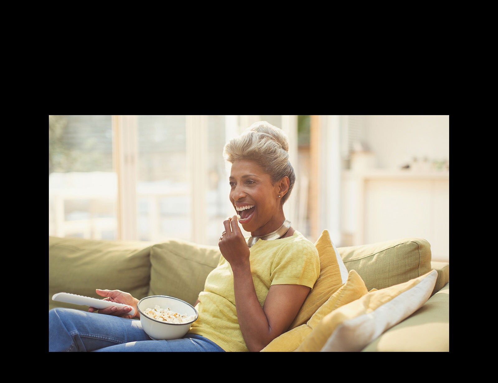 Naine vaatab telekat ja hoiab kaugjuhtimispulti käes. Ta sööb popkorni.
