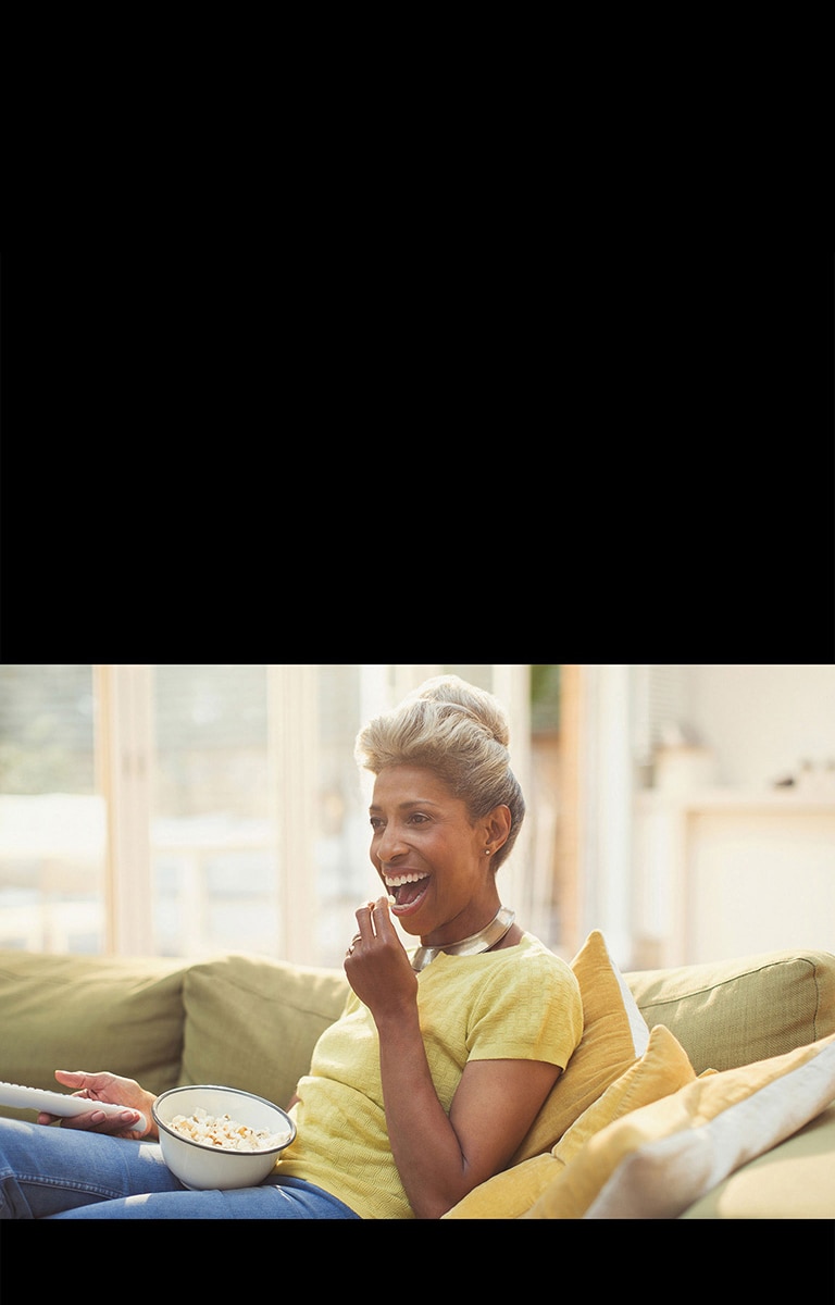 Naine vaatab telekat ja hoiab kaugjuhtimispulti käes. Ta sööb popkorni.