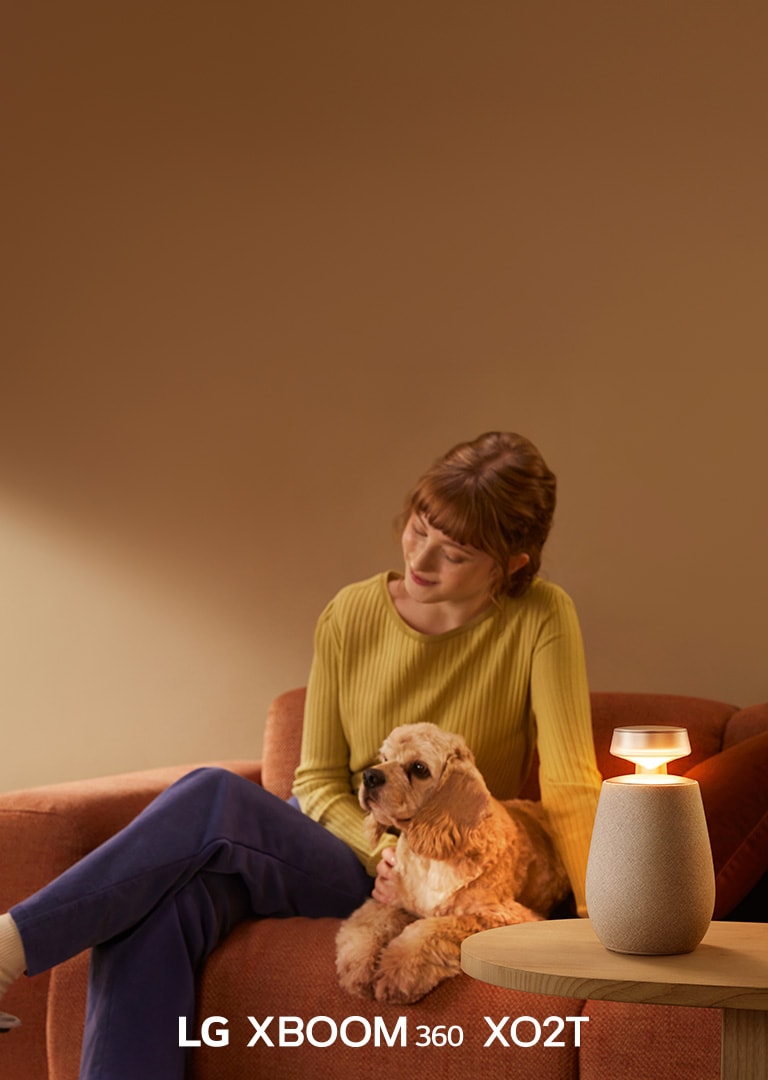 Naine istub koeraga diivanil ja kuulab LG XBOOM 360 XO2T-ga muusikat.