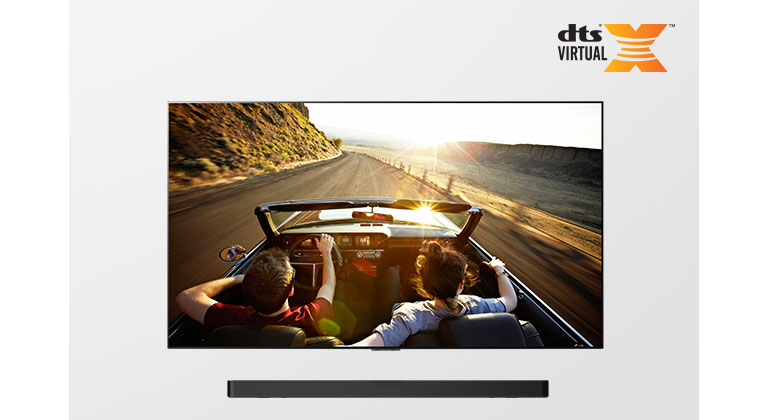 TV and Soundbar together in full view. TV shows a couple in an open roof car on the road driving into the sunset. 