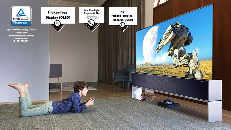 Põrandal lebades juhtkangi hoidev ja teleriekraanil mängu mängiv laps