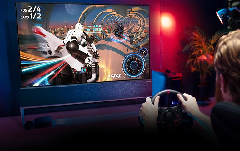 Mänguri võidusõidutoolis istuv ja rooliratast hoidev mees, kes mängib teleris kihutamismängu