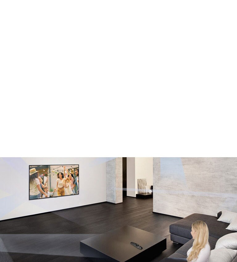 امرأة تجلس في غرفة معيشة رحبة تتميز بديكور داخلي بسيط وتشاهد أشخاصًا يرقصون على شاشة التلفزيون