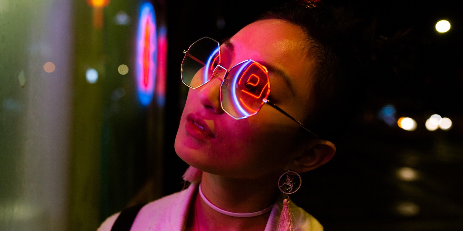 A close up of a woman wearing sunglasses with neon lights reflecting on her.