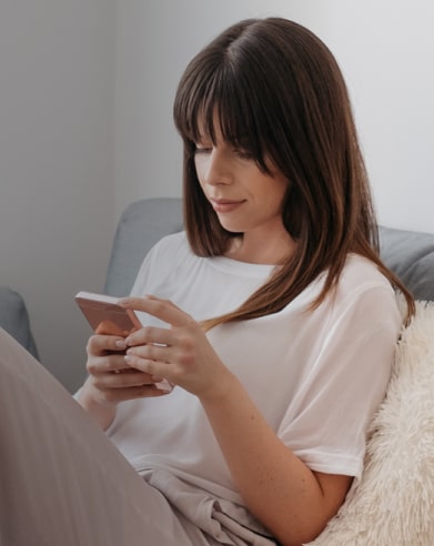 A woman is sitting on the sofa and looking at her phone.